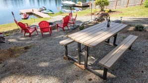 A picnic table with benches, surrounded by red chairs, near a lake with boats docked.