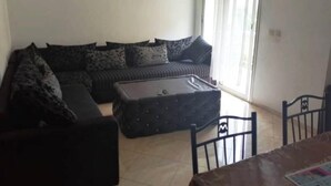 A living room with a sectional sofa, a small ottoman, and a dining table with chairs. - Nice apartment in Essaouira 4267 (Essaouira)