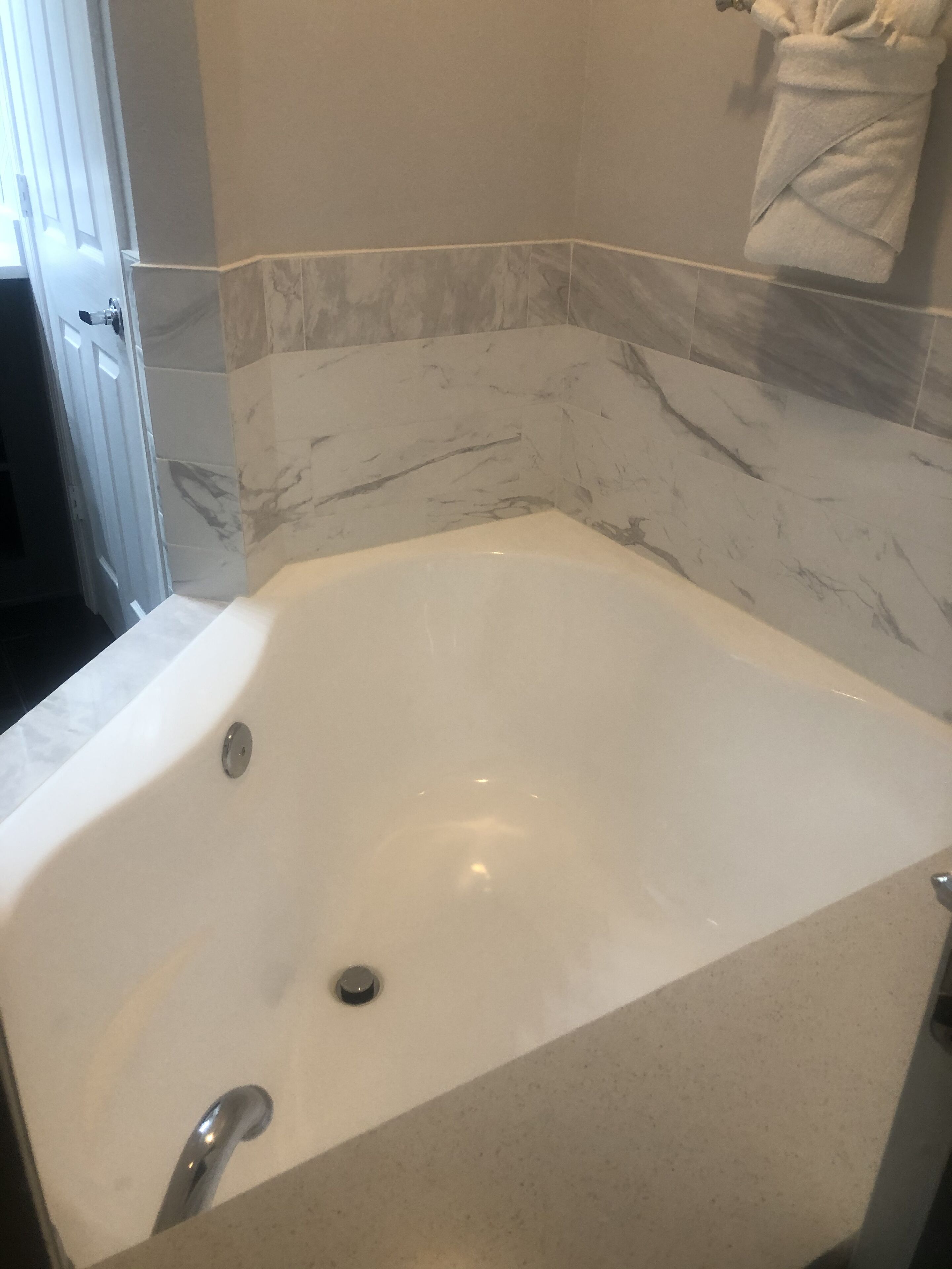 A bathroom with a large bathtub, marble walls, and a towel rack.