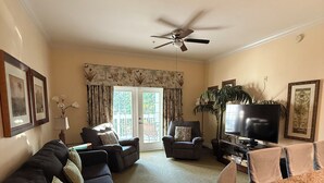 Un salon comprenant un canapé, des fauteuils, une table à manger, un téléviseur et un ventilateur de plafond.