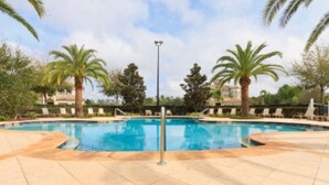 Une piscine dotée d’une terrasse carrelée, entourée de palmiers et de chaises longues.