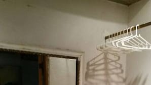 Ein kleiner, schummrig beleuchteter Raum mit einem Fenster, einem Heizkörper und einer Kleiderstange.