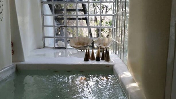 Ein kleiner Innenpool mit klarem Wasser, ein weiß gefliester Boden und ein Fenster mit einem Metallgitter.