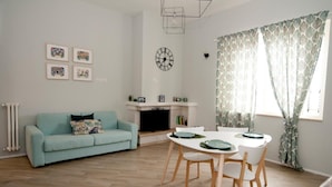 A living room with a light blue sofa, a white dining table with chairs, a fireplace, and a clock on the wall. - Le Fontanelle B&B (Sarno)