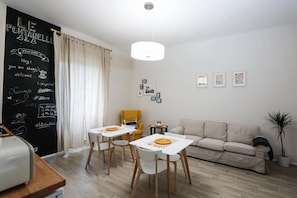 A modern living room with a dining area, a sofa, a yellow armchair, and a blackboard with writings.