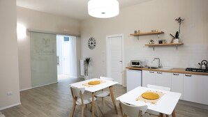 A modern kitchen with white cabinets, a stove, and a microwave. There are two white dining tables with chairs. - Le Fontanelle B&B (Sarno)