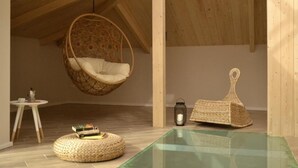 A cozy room with a hanging chair, a small table with books, a lantern, and a woven pouf. - Le Fontanelle B&B (Sarno)