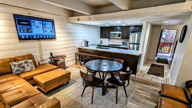 Una cocina moderna con televisor de pantalla plana, un comedor con mesa y sillas redondas, y una zona de estar acogedora con sofá y reposapiés.