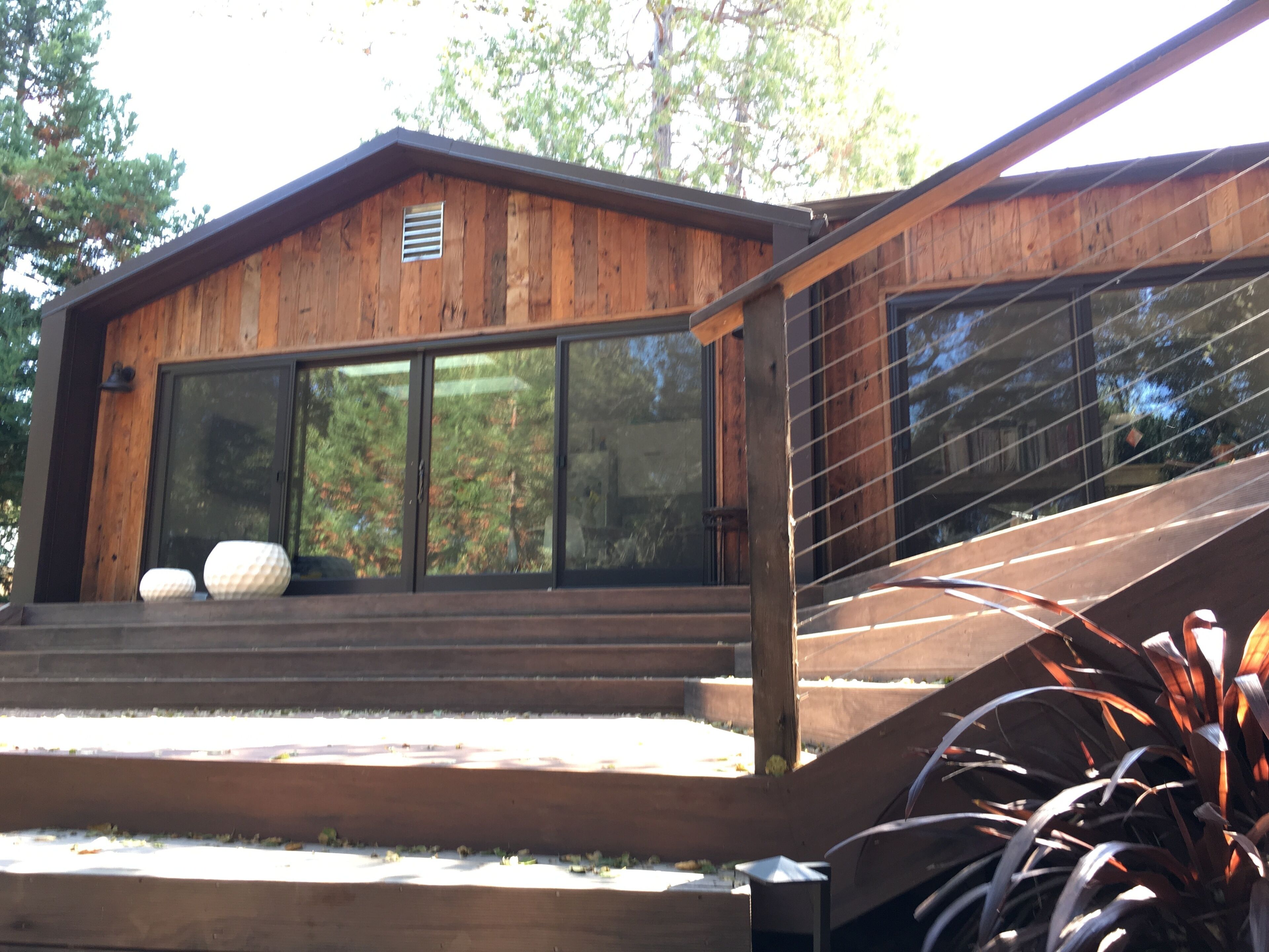 A wooden cabin with large sliding glass doors, a wooden deck, and a staircase leading to the entrance.