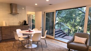 A modern kitchen with a dining area, a large sliding glass door leading to a balcony with a view of trees.