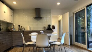 A modern kitchen with white cabinets, a central island, and a dining area with white chairs.