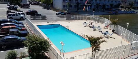 A swimming pool with a fenced deck, lounge chairs, and a view of the water.