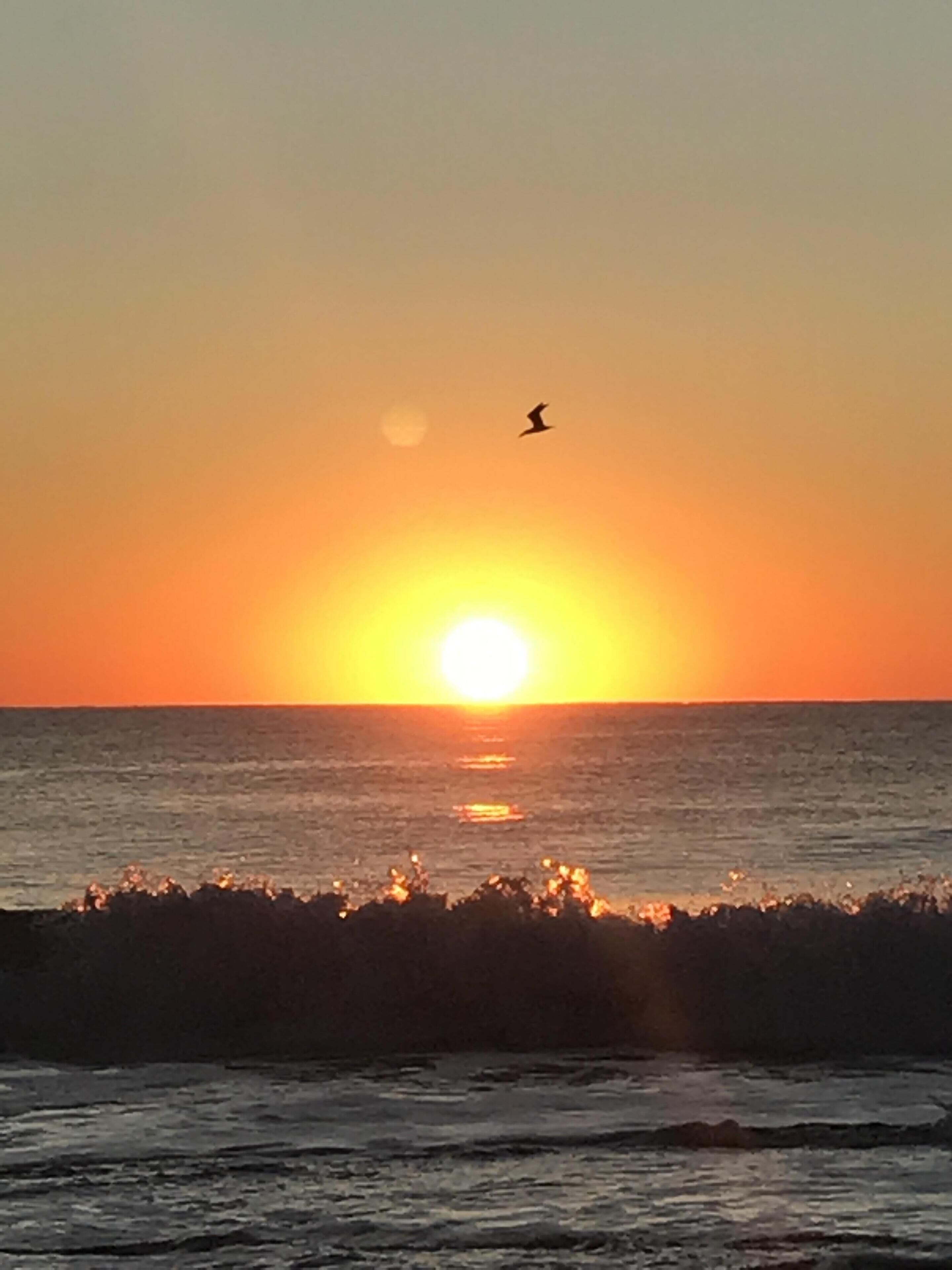 Um pôr do sol sobre o oceano, com ondas quebrando na praia.