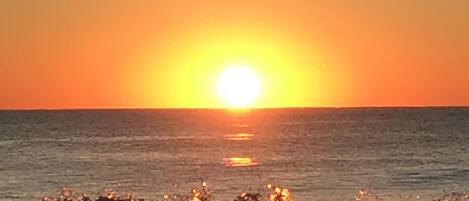 Um pôr do sol sobre o oceano, com ondas quebrando na praia.