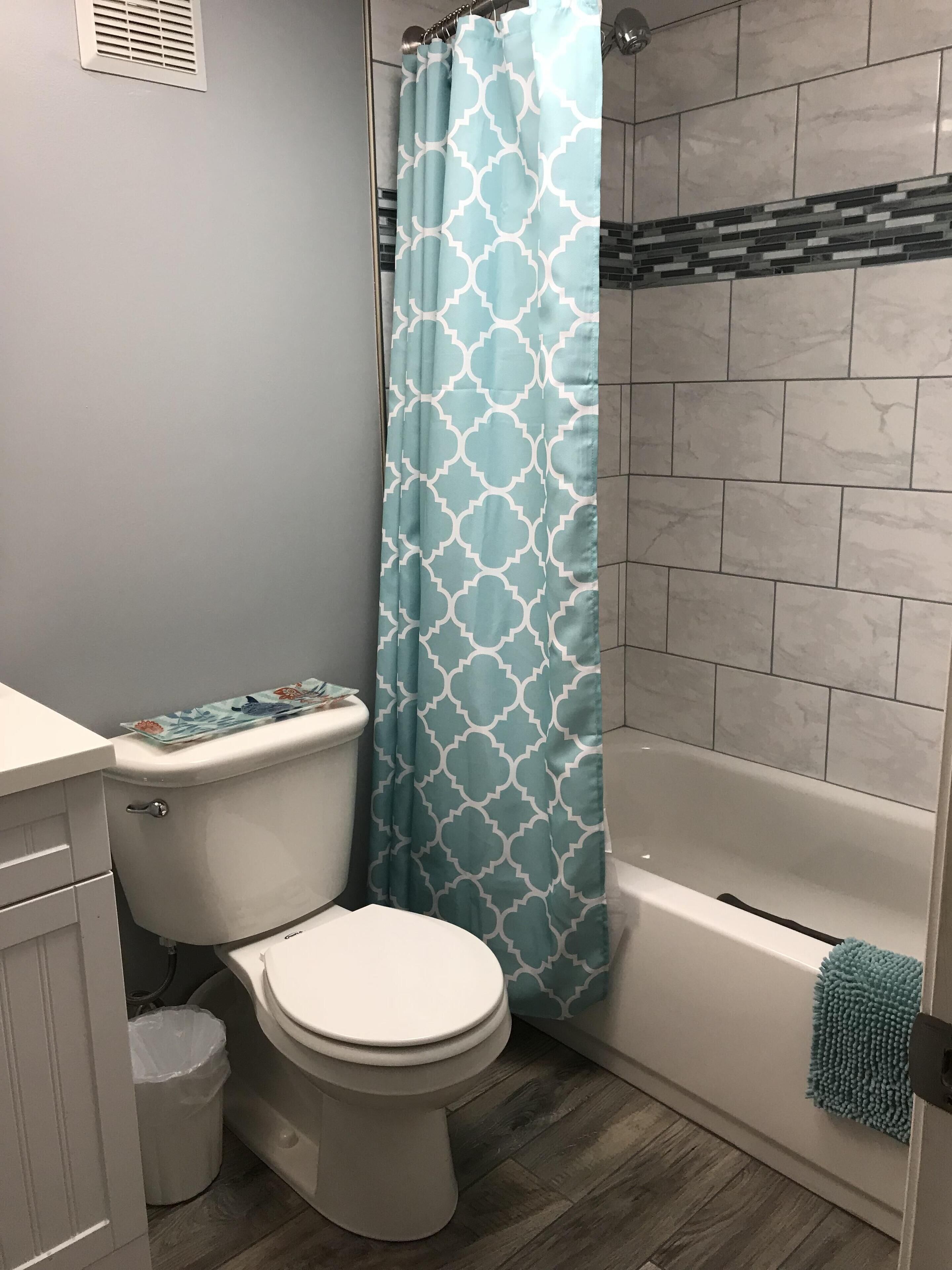 Ein Badezimmer mit Toilette, Duschvorhang, Badewanne und Mülleimer.