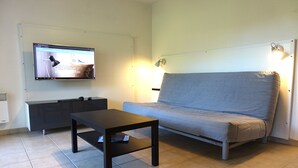 Ein Zimmer mit grauem Sofa, einem schwarzen Couchtisch, einem flachbildfernseher an der Wand und einem Schrank.