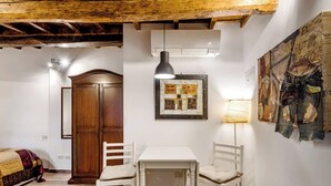 A room with a wooden ceiling, a white table with chairs, a framed picture, and a wall-mounted air conditioner.