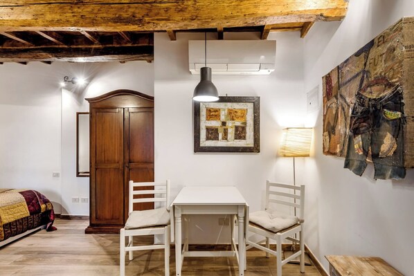Una habitación con techo de madera, una mesa blanca con sillas, un cuadro enmarcado y un aire acondicionado instalado en la pared.