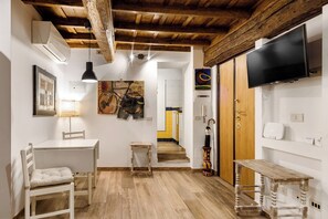 Una habitación con techo de madera, paredes blancas, un televisor montado en la pared, una mesa con una silla y una escalera que conduce a otra habitación.