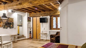 A room with a wooden ceiling, a bed with a patterned blanket, a television, and a small table.