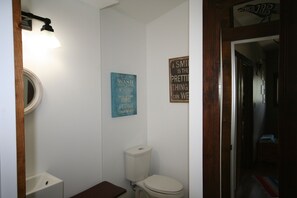 Une petite salle de bain avec des toilettes, un lavabo et un miroir. Deux panneaux sont accrochés au mur : l’un affiche les règles à respecter dans la salle de bain, et l’autre, une citation inspirante.