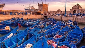A harbor filled with blue boats, a stone tower, and a building with a pointed roof. - Beautiful apartment in Essaouira 4266 (Essaouira)