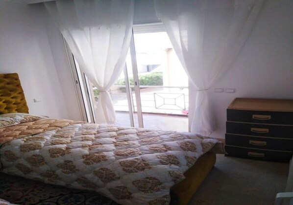 A bedroom with a bed, a dresser, and a sliding glass door leading to a balcony.