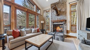 A cozy living room with a stone fireplace, a large window, and a mounted deer head.