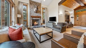 A spacious living room with a stone fireplace, leather sofas, a coffee table, and a mounted deer head.