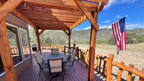Una terraza de madera con una mesa, sillas, una bandera y vistas a las montañas.