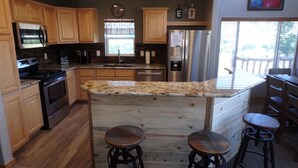 Una cocina con armarios de madera, un refrigerador de acero inoxidable, una isla integrada con taburetes y una ventana con vista al exterior.