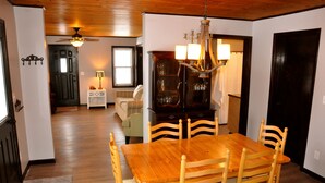 A dining area with a wooden table and chairs, a chandelier, and a cabinet with glassware.