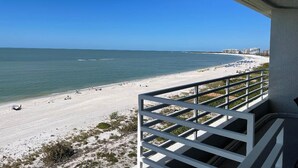 En vy över stranden från en balkong med ett räcke, med utsikt över en sandstrand och havet.