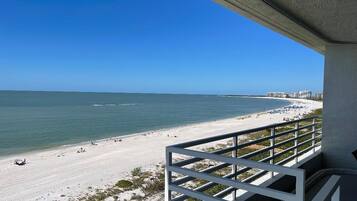 A beach view from a balcony with a railing, overlooking a sandy beach and the ocean.