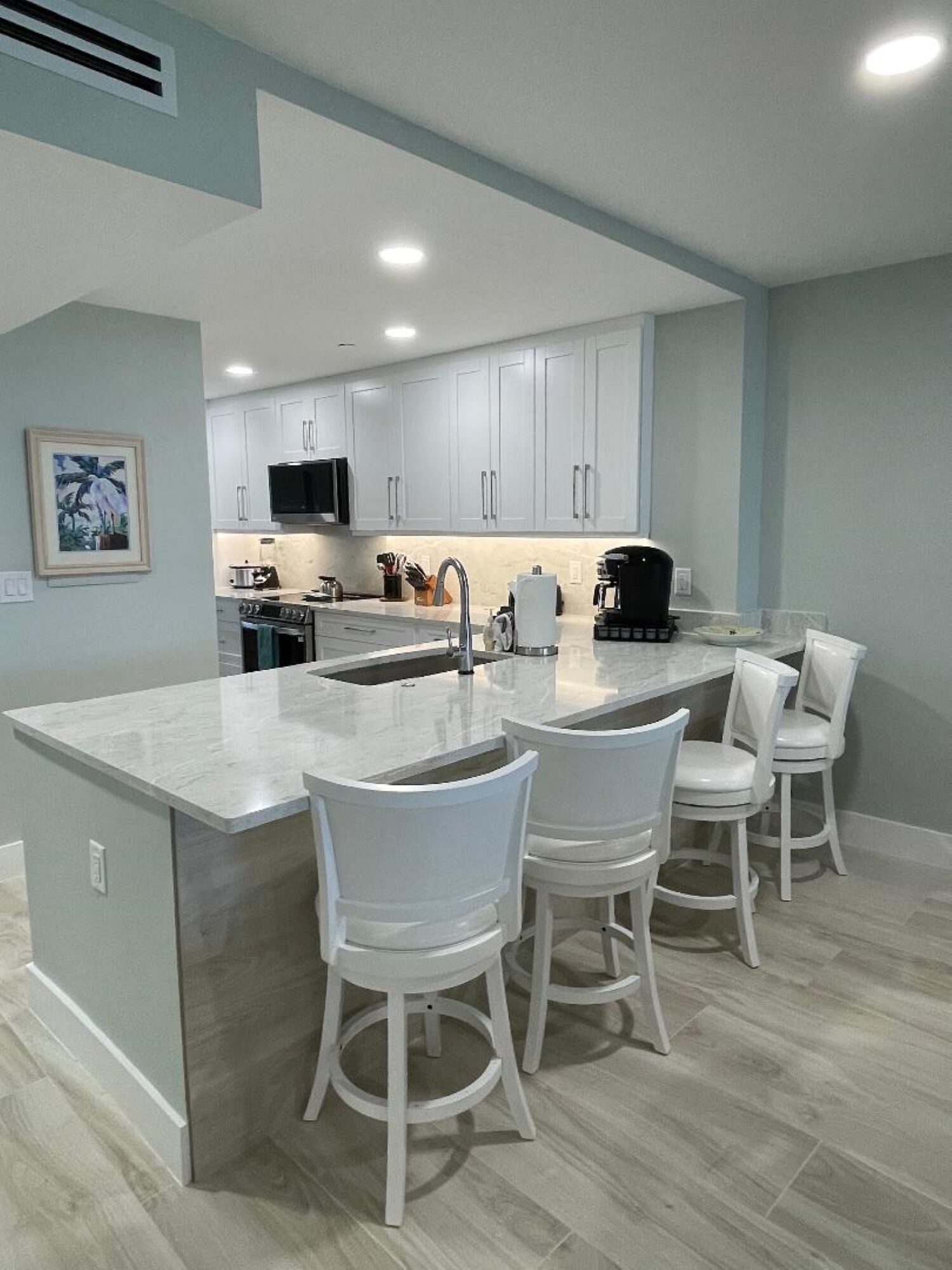 A modern kitchen with white cabinets, a central island with bar stools, and a microwave.