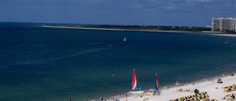 A beach with a sandy shore, a few sailboats, and a distant building.