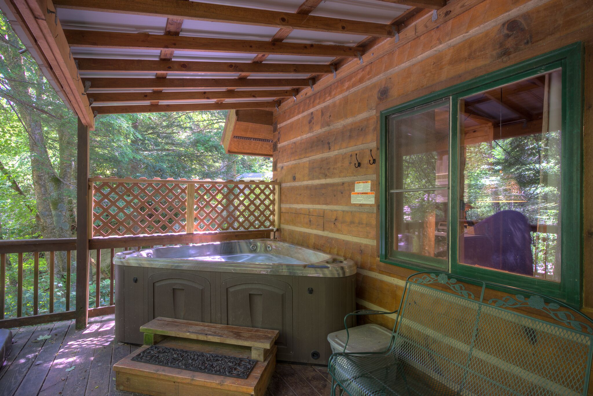 A wooden cabin with a hot tub, a wooden bench, and a metal chair on a deck.