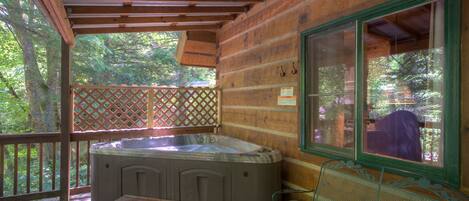 A wooden cabin with a hot tub, a wooden bench, and a metal chair on a deck.
