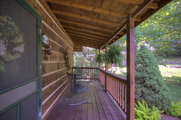 A wooden deck with a table and chairs, surrounded by greenery and a view of trees.