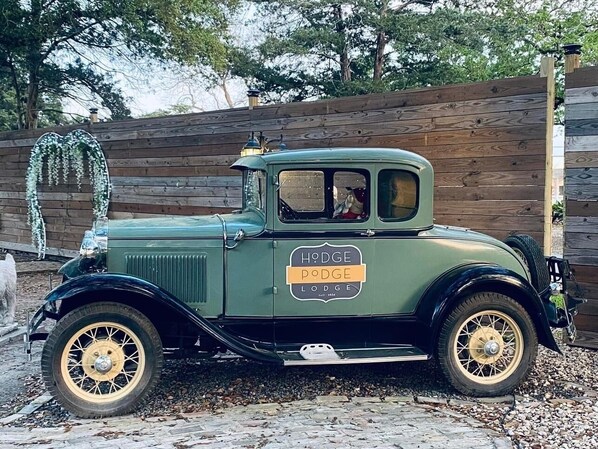 A vintage green car parked in front of a wooden fence with a sign that reads 'Hodge Lodge.' - Peaceful Suite Serenity (Montgomery)