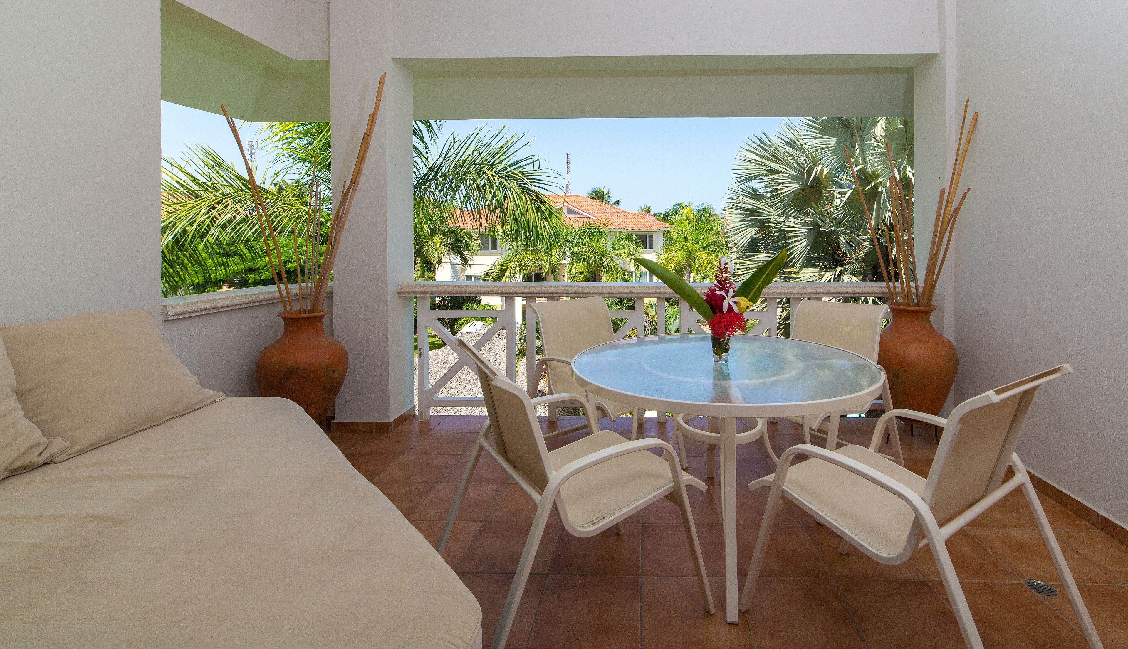 A balcony with a round table, white chairs, a sofa, and potted plants.