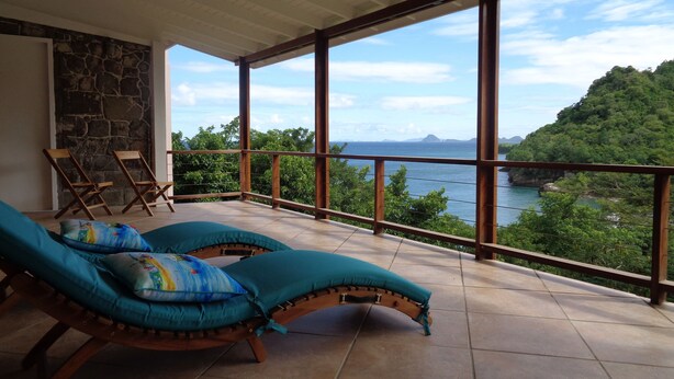 Un balcón con dos sillones, un muro de piedra y vistas al paisaje costero.