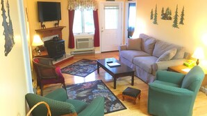 A living room with a sofa, two armchairs, a coffee table, a fireplace, a television, and a door with curtains. - Nordic Inn, Save 20% on Gorgeous 2BR, 2BA Condo! (Lincoln)