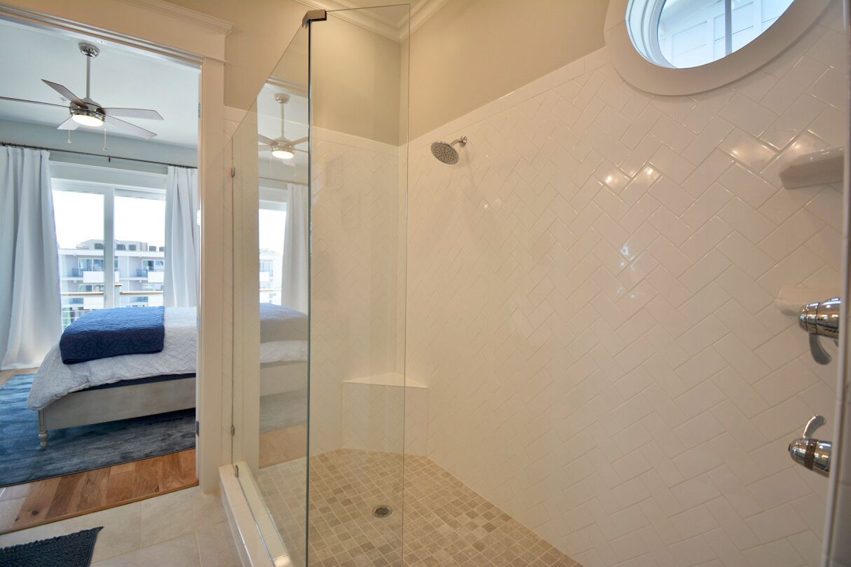 Une salle de bain moderne avec une douche à l’italienne en verre, des murs recouverts de carreaux blancs et une fenêtre ronde.