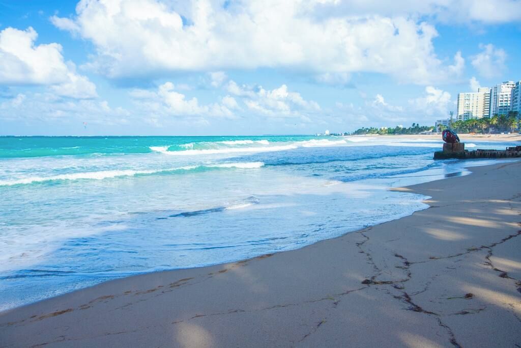 Una playa con olas, una escultura y edificios al fondo.