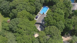Vista aérea de una propiedad con piscina rectangular rodeada de exuberante vegetación.