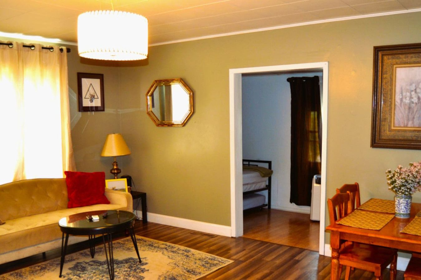 A living room with a sofa, a small table, a lamp, a mirror, and a dining area with a table and chairs.