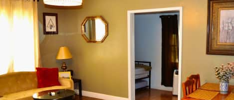 A living room with a sofa, a small table, a lamp, a mirror, and a dining area with a table and chairs.