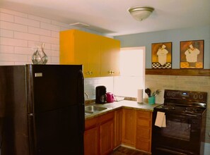 A kitchen with a black refrigerator, wooden cabinets, a yellow upper cabinet, a stove, and a sink.
