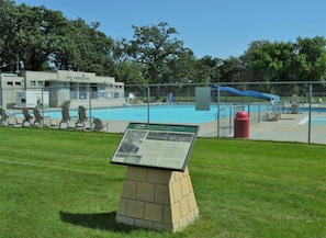 A community park with a swimming pool, a fenced area, and a brick monument with an informational plaque.